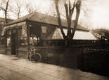 A bicycle leans on the fence outside our small original location, circa 1910
